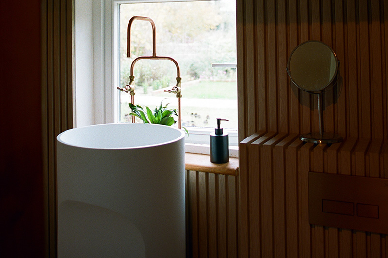 En-suite with sculptural round basin, copper tap and fluted oak panelling