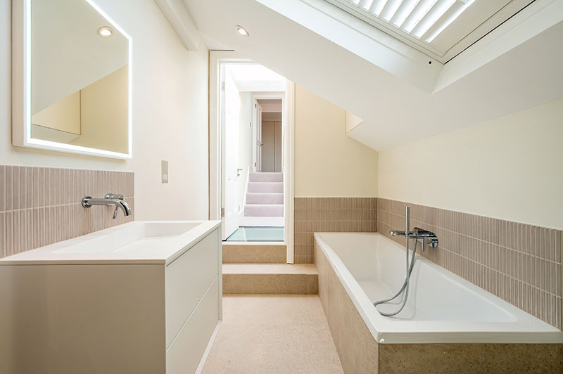 Loft bathroom with skylight, stone-clad bath and floating vanity unit