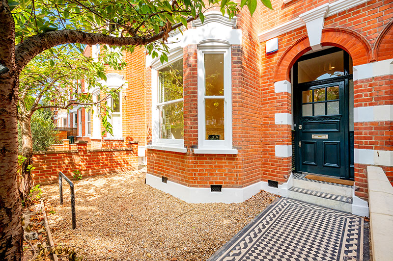 Red brick Victorian terrace frontage with restored black front door and mosaic tiled path