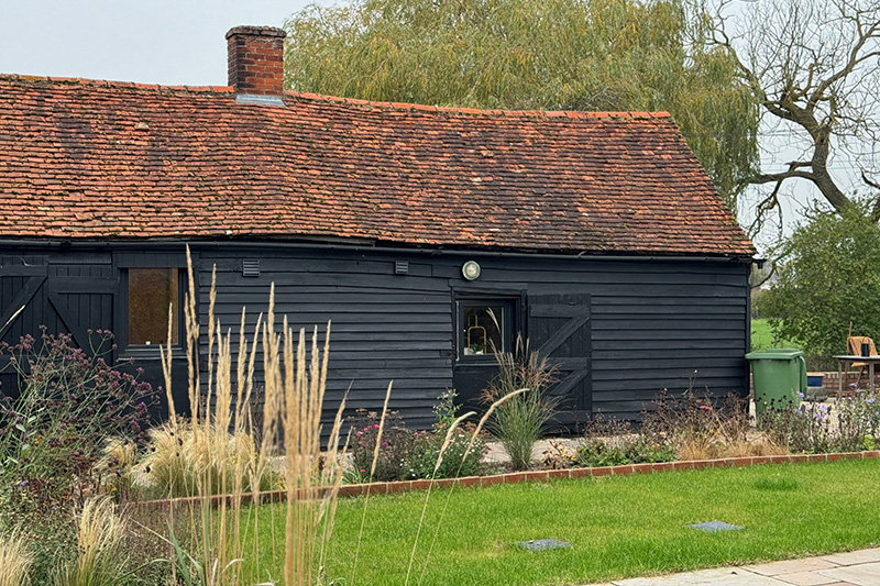 Original black weatherboarded barn with pantile roof and planted garden borders