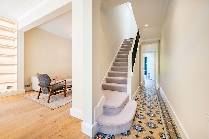 Entrance hallway with original patterned floor tiles, carpeted staircase and open-plan living room