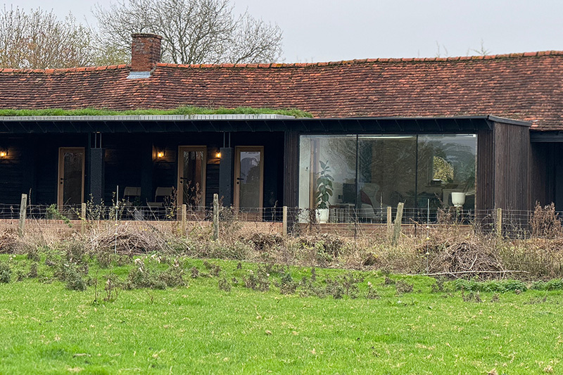 Long barn elevation with clay tiled roof and picture window set in dark timber cladding