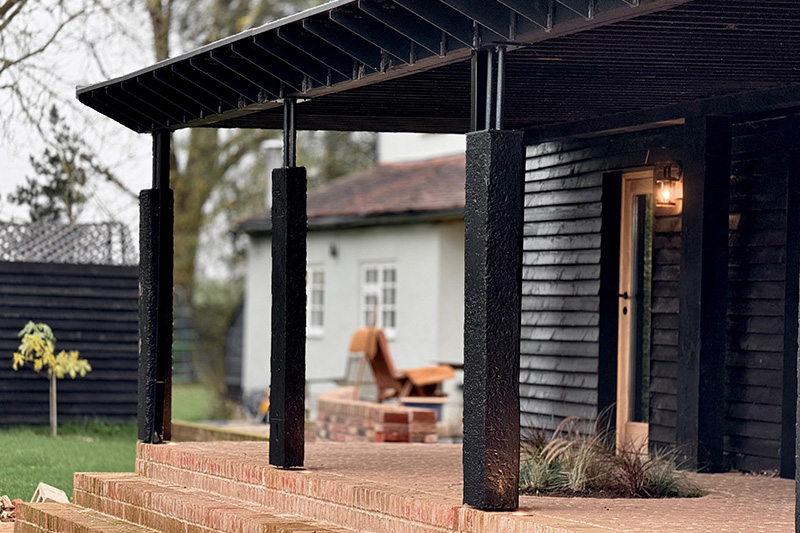 Charred timber posts supporting the covered veranda above brick paved steps