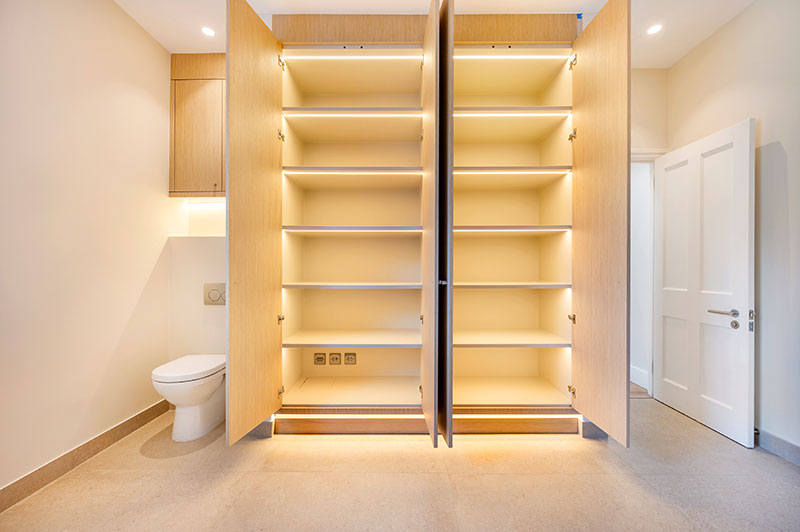 Bespoke illuminated storage joinery beside a concealed cloakroom